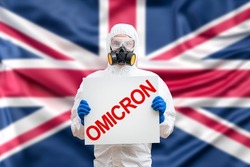 Medical worker wearing PPE protective white suit,face shield mask, holding text inscription omicron covid-19 Coronavirus subtype or stealth omicron BA.2 new variant behind blur uk united kingdom flag