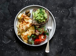 Delicious healthy breakfast - omelette, vegetables, avocado toast on a dark background, top view