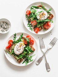 Wholegrain bread sandwiches with avocado, poached egg and arugula cherry tomatoes salad - delicious healthy breakfast, brunch on a light background, top view      