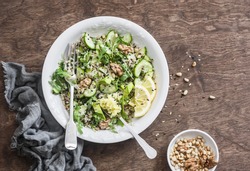 Quinoa and greens veggies salad for a spring detox. Salad with quinoa, cucumbers, avocado, arugula, ginger, flax seeds and nuts on wooden background, top view. Mediterranean style food concept