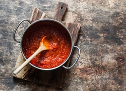Classic homemade tomato sauce in the pan on a wooden chopping board on brown background, top view. Pasta, pizza tomato sauce. Vegetarian food 