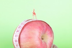 Miniature female doll model standing on an apple doing slimming exercises