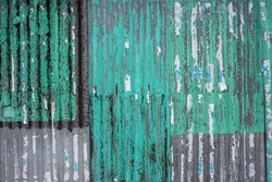 Texture of a weathered corrugated iron wall in gray and with. The sheet metal cladding is aged and the remains of posters are stuck to the facade.