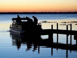 The Silhouette of Three Retired Fisherman Heading Out for a Day of Fishing at Sunrise in Their Pontoon Boat 