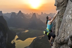 Female extreme climber conquers steep rock against the sunset over the river. China, typical Chinese landscape with mountains and river.