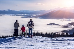 People observing mountain scenery.
Family of three people stays in front of scenic landscape. These are skiers, they dressed in winter sport jackets and have skies attached.