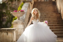 A naughty blonde bride, with cool make-up in a wedding dress. Stands against the background of the old church and smiles. Bride beautiful wedding flowers bouquet, gorgeous woman. Husband and wife.