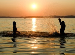Girl and boy swimming in the lake at sunset, splashes of transparency water, female an male silhouette.