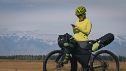 The woman travel on mixed terrain cycle touring with bikepacking. The traveler journey with bicycle bags. Sportswear in green black colors. Mountain snow capped. Make a selfie smartphone
