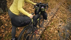The woman travel on mixed terrain cycle touring with bikepacking. The traveler journey with bicycle bags. Sportswear in green black colors. The trip in magical autumn forest. Wooden bridge, river.