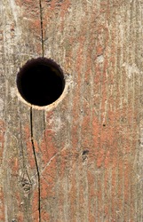 An old weathered board with fading paint and a round hole.