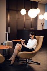 Confident businesswoman listening music on her tablet computer while sitting in chair in airport business lounge