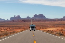 Motorhome roadtripping with Monument Valley behind under blue sky