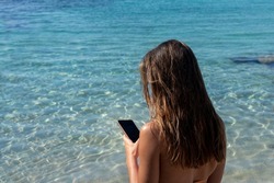 Back view of half body young brunette unrecognizable woman on bikini at the beach with clear turquoise water