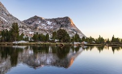 High altitude alpine lake with reflection and calm water during dusk on a summer evening while backpacking in Yosemite National Park, California, USA
