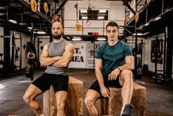 Two men sit on wooden boxes and look at the camera. Resting after a hard workout.