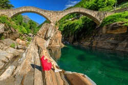 Ponte dei Salti Roman stone bridge over Verzasca River. Verzasca valley by Lavertezzo town. Famous landmark in canton of Switzerland. Woman sunbathing in Switzerland nature park.