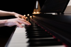 Hands playing the piano keyboard closeup and candle light bokeh background. Male pianist learning to play the piano instrument and beautiful music. Reading sheet music