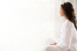 Serene woman in bathrobe meditating at sunny window