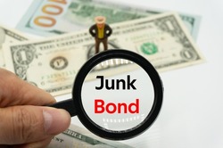 Junk Bond.Magnifying glass showing the words.Background of banknotes and coins.basic concepts of finance.Business theme.Financial terms.