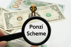Ponzi Scheme.Magnifying glass showing the words.Background of banknotes and coins.basic concepts of finance.Business theme.Financial terms.