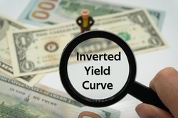 Inverted Yield Curve.Magnifying glass showing the words.Background of banknotes and coins.basic concepts of finance.Business theme.Financial terms.
