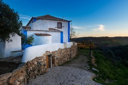 View of a traditional house painted in white and blue, with agricultural fields on the background, near Mafra, Portugal.