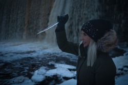 A girl at the Jagala waterfall in Estonia holds an icicle like a knife and swings it at dusk.