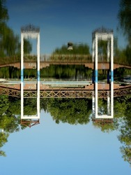 In the photo there is a lake and the bridge , with the reflection of it with the sky. The photo is upsidedown