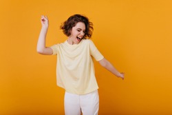 Pale brown-haired girl in yellow t-shirt dancing with inspired face expression. Active young woman in casual summer outfit having fun indoor.