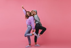Full-length photo of inspired girls funny dancing together. Indoor shot of cheerful best friends standing on bright background.