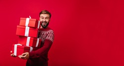 Blithesome bearded white guy enjoying christmas time with presents. Indoor shot of carefree european man in red sweater having fun at new year party.