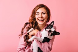Wonderful european female model chilling in studio with puppy. Indoor portrait of debonair girl enjoying photoshoot with her cute pet.
