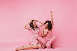 gentle and lovely girls with black curly hair, in pink pajamas having fun and raising their hands, dancing in front of camera