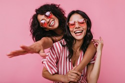 Unrestrained merriment of two girls captured on snapshot. Photos in pink shades of brunettes with beautiful curls, embracing in friendly way