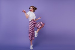 Inspired jocund girl in sneakers dancing on purple background. Gorgeous young female model with dark wavy hair jumping in studio.