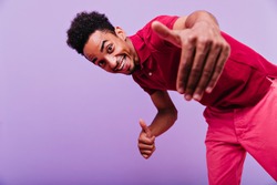 Excited black male model dancing in studio. Funny emotional man in red t-shirt looking to camera with smile.