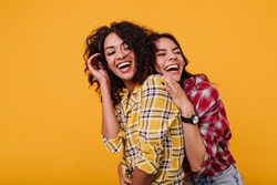 Girls in stylish street clothes sincerely laugh at each other's jokes. Girlfriends happily pose for common photo in studio