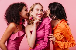 Studio portrait of three international friends smiling on pink background. Half length photo of girls sharing news.
