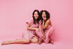 two girls with dark hair, one with straight and other with curly, dressed in soft and lovely pajamas, having fun and playing, looking at camera