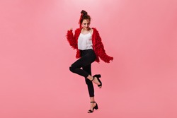 Nice woman in woolen jacket and black pants dancing on pink background