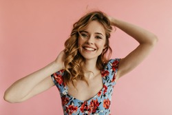Portrait of blond curly haired woman in blue floral top looking into camera and smiling on isolated backdrop. Modern girl in summer t-shirt posing..