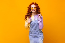 Red-haired lady in denim sundress and multi-colored sweatshirt laughs on orange background