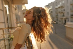 light relaxing image of girl in glasses close-up under sun's rays. Stands on balcony and extends her long hair to sides. She likes to bask in sun.