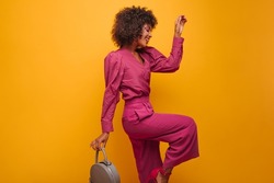 profile photo of spectacular African woman in fashionable lilac suit on isolated background. dark-haired woman with short curly hair posing elegantly with handbag in her hands.