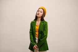 Feminine young caucasian fashion model in autumn clothes and hat posing in studio with space for text. Brunette woman is wearing bright green jacket and yellow beret. Stylish girl concept