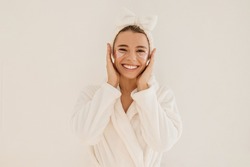 Happy young caucasian woman in bathrobe and cosmetic hair bandage smiling looking at camera on white background. Blonde uses hydrogel patches under holes. Home spa concept