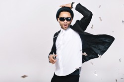 Positive excited handsome guy in suit, hat, black sunglasses having fun on white background. Listening to music through headphones, dancing, singing, celebrating party, happiness