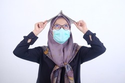 portrait of a Muslim woman wearing a mask with a confused gesture carrying a school book