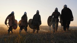 Warriors vikings stand in field and look at beautiful sunset on the battle field. Medieval Reenactment.Contre-jour. Back view.